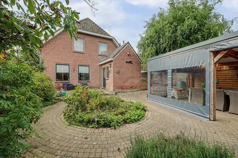 Besloten achtertuin met klinkerterras, ronde border, serre en de achterzijde van de woning
