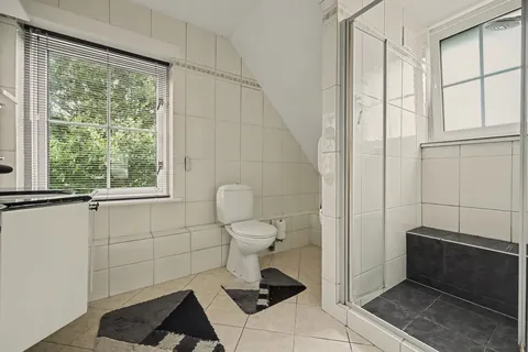 Betegelde badkamer met douchecabine, toilet en raam