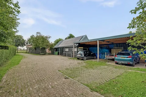 Houten carport met ruimte voor meerdere auto's en de trailer, naast de schuur