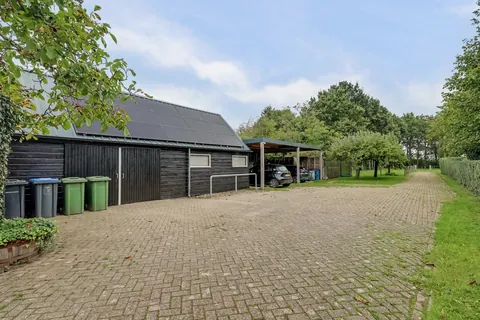 Gepotdekselde zwarte schuur met 15 zonnepanelen op het dak en de carport ernaast