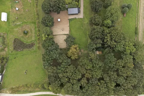 Luchtfoto recht van boven van de rijbak, de stal en de weides tussen de bomen