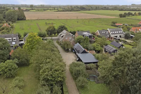 Luchtfoto van de woning, de schuur met zonnepanelen en de carport, met de polder aan de overkant van de weg