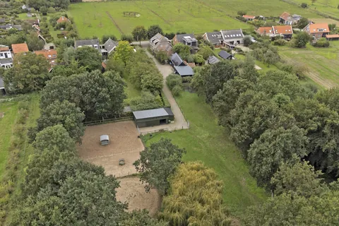 Luchtfoto van de stal en de rijbak met het dorp Nisse op de achtergrond