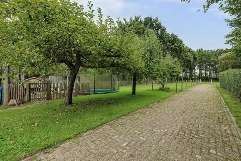 Klinkerpad langs fruitbomen, de kippenren en de ingegraven trampoline richting de paardenstal