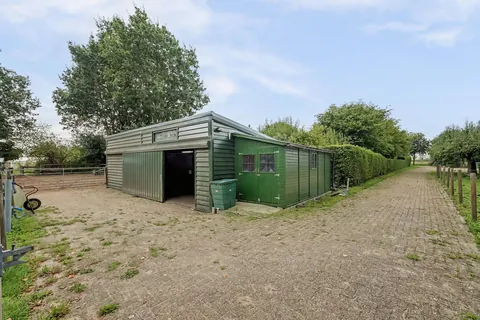 Groene paardenstal met schuifdeur en aangebouwd stro- en hooihok, naast de rijbak