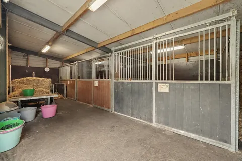 Binnen in de paardenstal: drie boxen met stalen fronten en opslag voor hooi