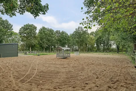 Zandbak van de rijbak met overdekte hooiruif en de groene paardenstal