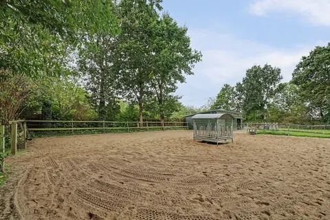 Zandbak van de rijbak met houten omheining en hooiruif onder volwassen bomen