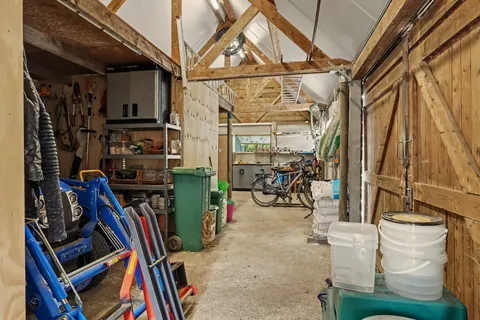 Binnen in de schuur van 12 bij 5 meter met houten spanten, betonvloer en werkbank