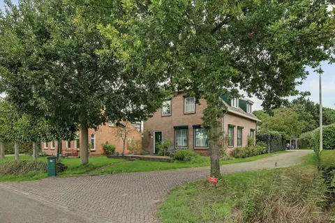 Voorzijde van de woonboerderij met de brede oprit naar de carport en schuur