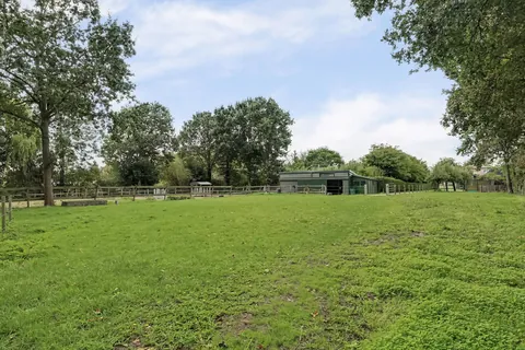 Groene weide met houten omheining en zicht op de paardenstal