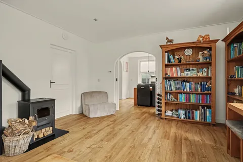 Woonkamer met houtkachel, deur naar de hal en boog naar de eetkamer